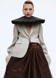 Model wearing a grey blazer, large structured black collar, and brown skirt against a white seamless background