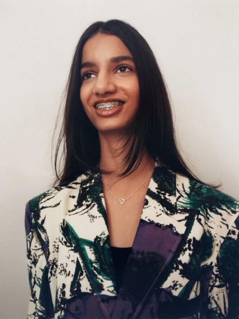 Portrait of a young woman with braces and a colorful blazer, set against a clean white backdrop, showcasing natural light and clear focus.