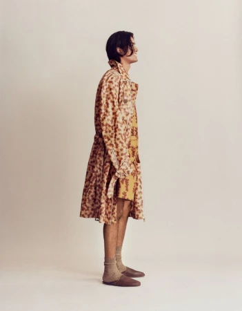 Model standing in profile wearing a patterned trench coat and brown loafers against a neutral backdrop.
