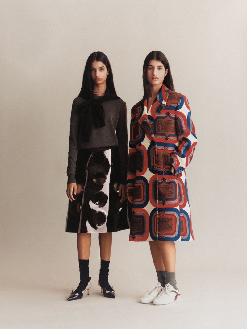 Two female models standing against a neutral studio backdrop wearing patterned and textured designer fashion apparel