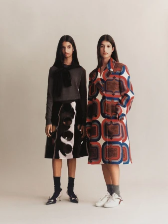 Two female models standing against a neutral studio backdrop wearing patterned and textured designer fashion apparel