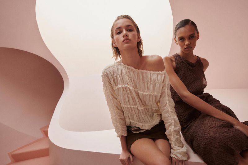 Two female models posing inside a modern architectural interior with curved pink walls for a Massimo Dutti campaign.