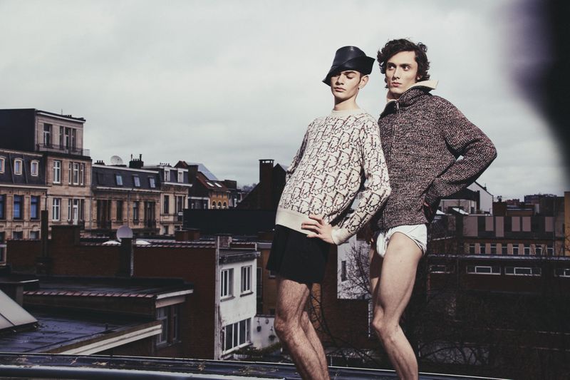 Two male models posing on a rooftop overlooking city buildings for Numero Netherlands editorial project Let's play like brothers do