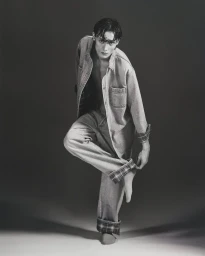 Young male model posing in denim shirt and cuffed trousers against a dark gradient studio background