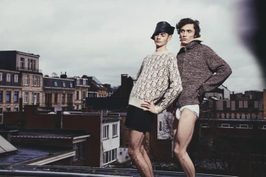 Two male models posing on a rooftop overlooking city buildings for Numero Netherlands editorial project Let's play like brothers do
