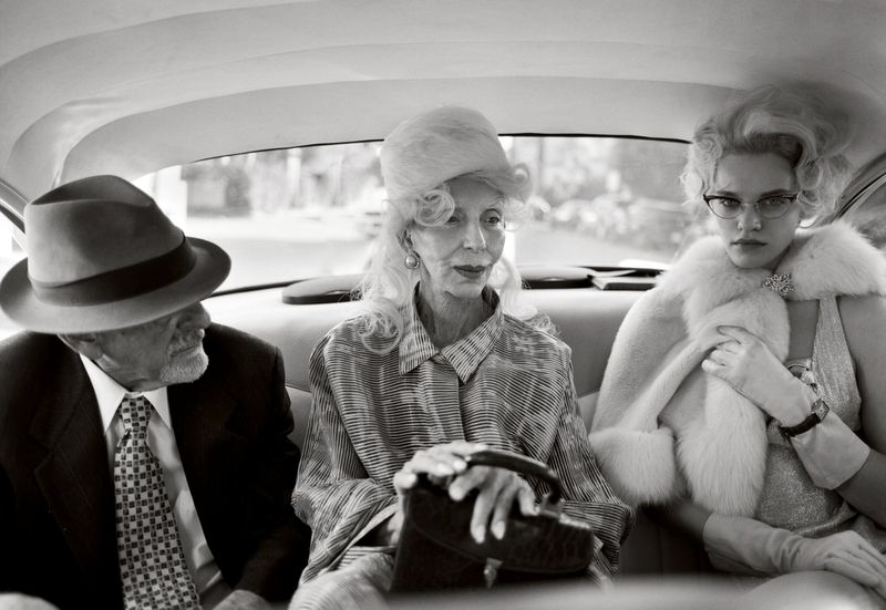 Black and white photo of three people in an automobile: an elderly man in a suit, an elderly woman in patterned shirt and a young woman.