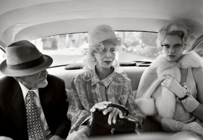 Black and white photo of three people in an automobile: an elderly man in a suit, an elderly woman in patterned shirt and a young woman.