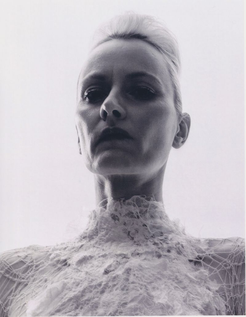 Monochrome portrait of adult woman with blond hair and ornate lace collar, captured with a low angle in bright studio lighting.
