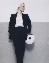 Model in a black suit holding a white helmet against a split grey and white studio wall