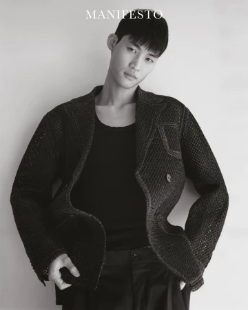 Man wearing a textured dark blazer and black tank top against a plain light background for Manifesto Magazine