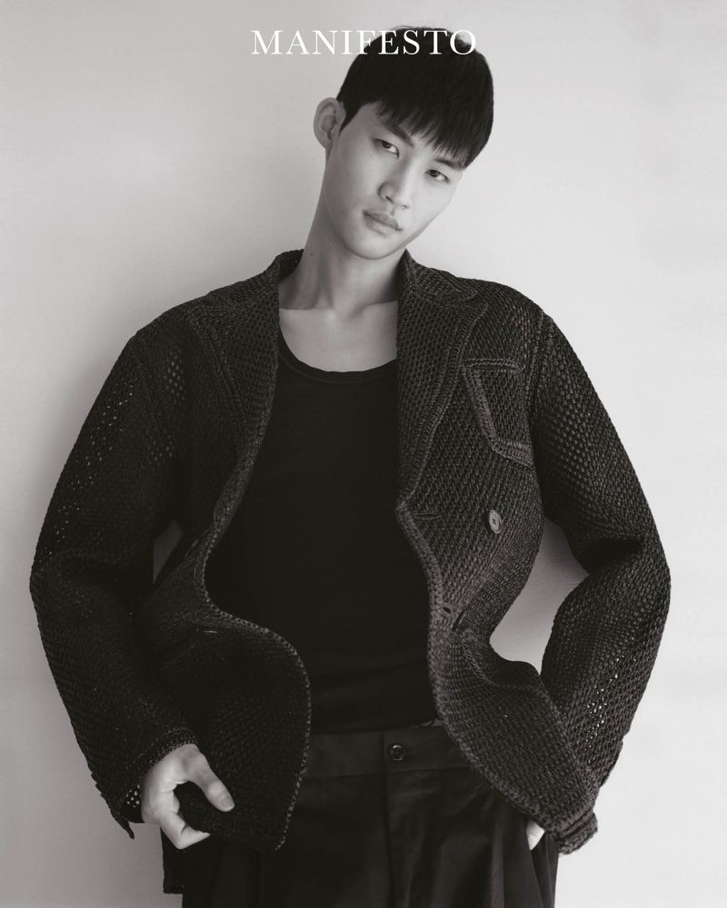 Man wearing a textured dark blazer and black tank top against a plain light background for Manifesto Magazine