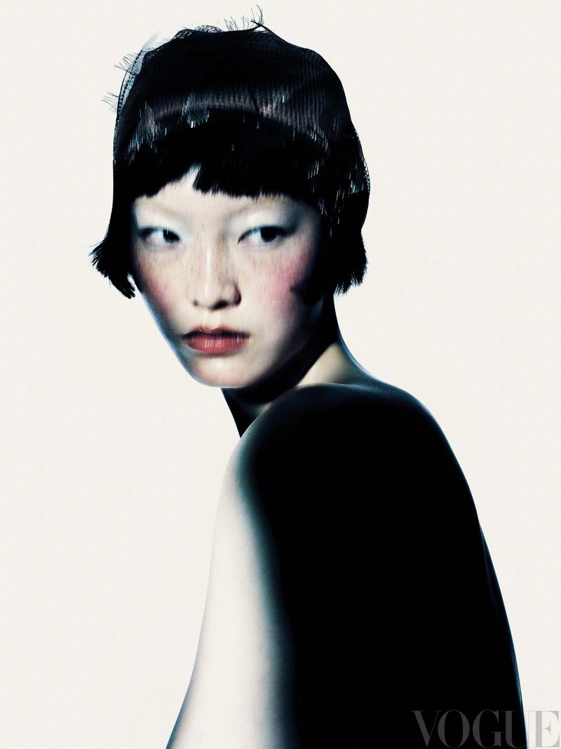 Beauty shot of an Asian female model with pale skin, dark bob haircut, and intense makeup in a stark studio setting with soft, diffused lighting.