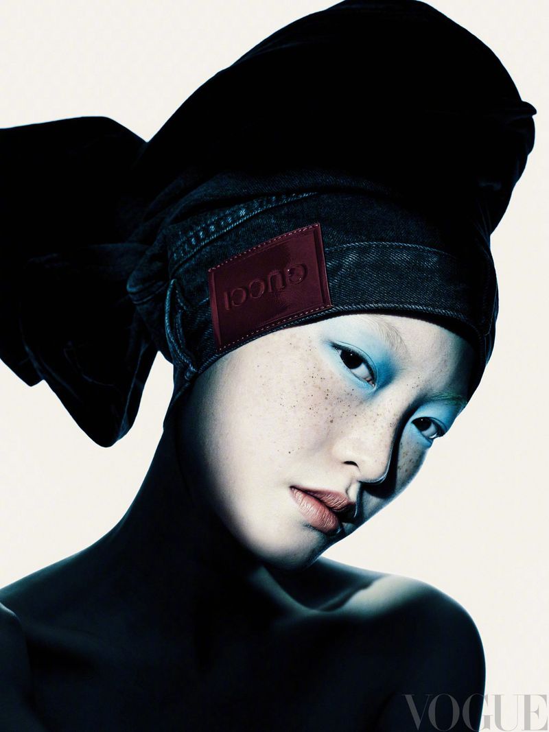 Close-up portrait of model Li Linzi wearing a large black headwrap with a red logo patch against a plain white background