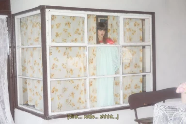 Lindsey Wixson looking out a multi-pane bay window with yellow floral curtains in a fashion editorial for Modern Weekly China.