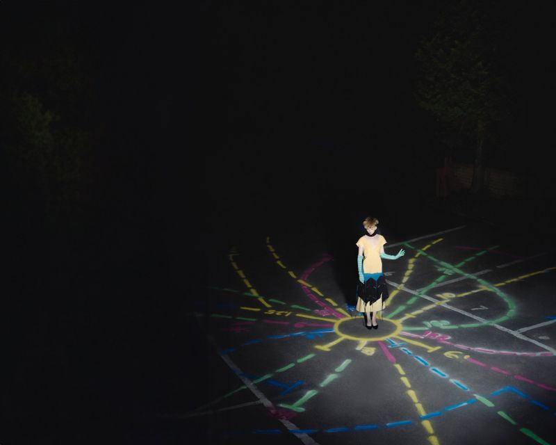Young person stands on illuminated chalk art in outdoor nighttime setting with trees and dark sky, creating a surreal and dreamy scene.