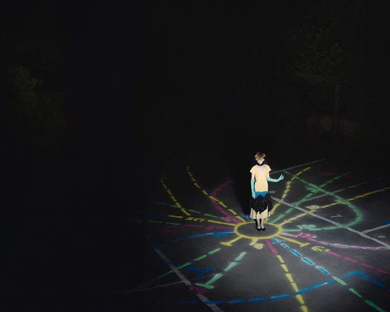 Young person stands on illuminated chalk art in outdoor nighttime setting with trees and dark sky, creating a surreal and dreamy scene.