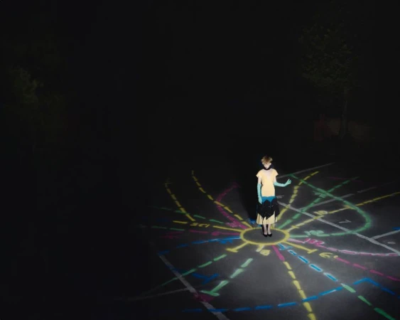 Young person stands on illuminated chalk art in outdoor nighttime setting with trees and dark sky, creating a surreal and dreamy scene.