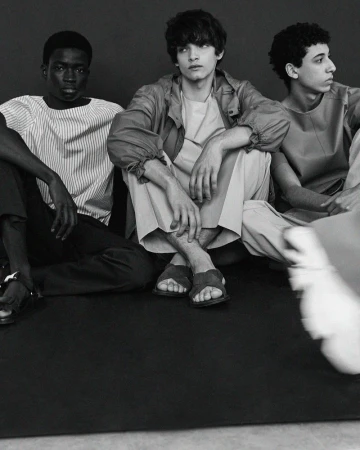 Black and white editorial portrait of three young men sitting together on the floor wearing lightweight casual apparel
