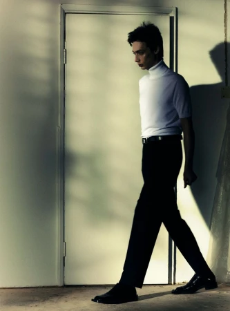 Model Bunny Syxes in a white turtleneck and black trousers walking past a closed door in an editorial portrait for The Greatest Magazine.