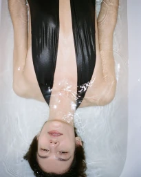 Model floating in a bathtub wearing a black plunging swimsuit for Christopher Esber Swim PF 24 campaign.