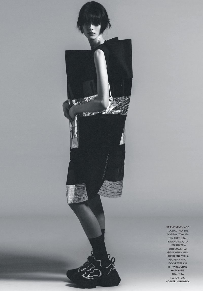 Model Leonie Steffen wearing a sculptural black structured garment and sneakers against a seamless grey backdrop.