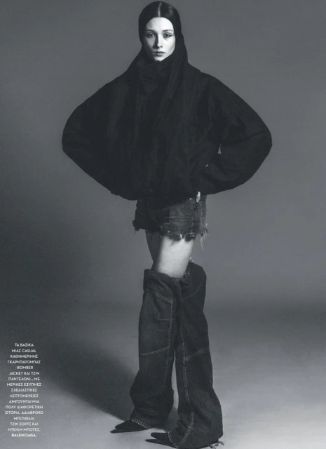 A full-length studio shot captures a fashion model in a black hooded jacket, denim mini skirt, and deconstructed denim boots against a grey backdrop.