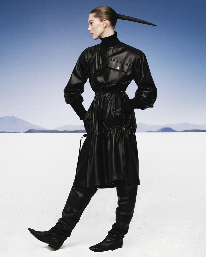 Fashion shot of a woman in a black leather dress and thigh-high boots, striking a pose against a clear blue sky and a white desert.