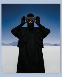 Model Iselin Steiro wearing all black holding custom optical eyewear against a white salt flat and blue sky horizon.