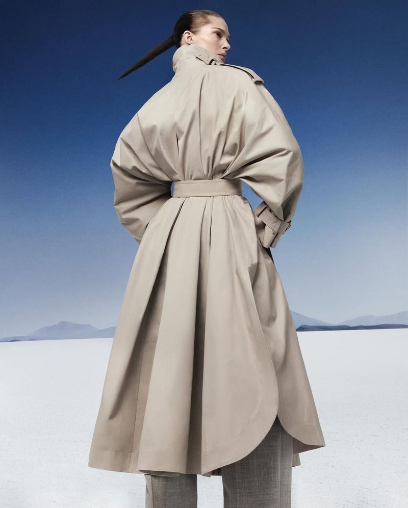 Model Iselin Steiro wearing a belted beige trench coat against a desert salt flat and blue sky for Mastermind Magazine.