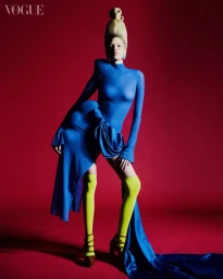 Model in a blue dress with high yellow socks and tall blonde updo against a red background for Vogue Brasil.