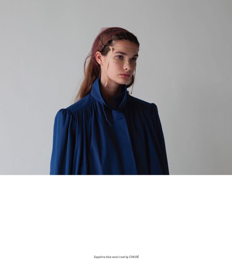 Fashion shot of a female model wearing a dark blue wool coat, set against a neutral backdrop in a photo studio, style editorial.
