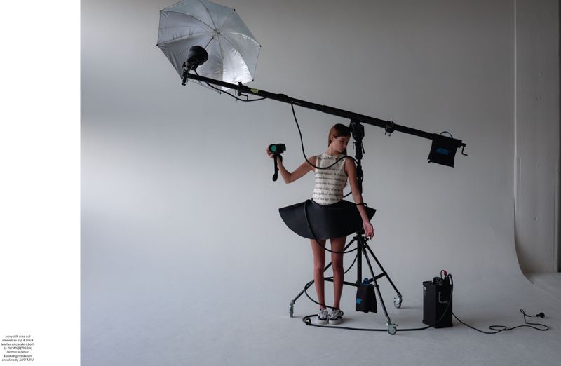 Woman poses in a tutu skirt in a photo studio under studio lighting equipment for a fashion shoot on a white seamless backdrop.