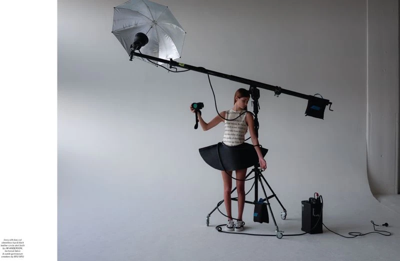 Woman poses in a tutu skirt in a photo studio under studio lighting equipment for a fashion shoot on a white seamless backdrop.