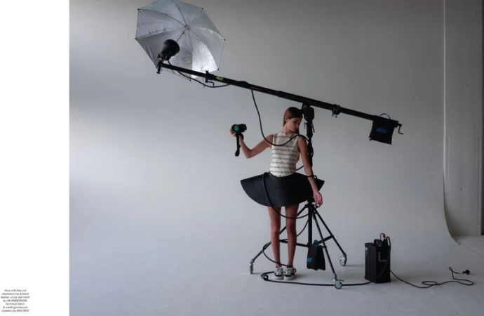 Woman poses in a tutu skirt in a photo studio under studio lighting equipment for a fashion shoot on a white seamless backdrop.