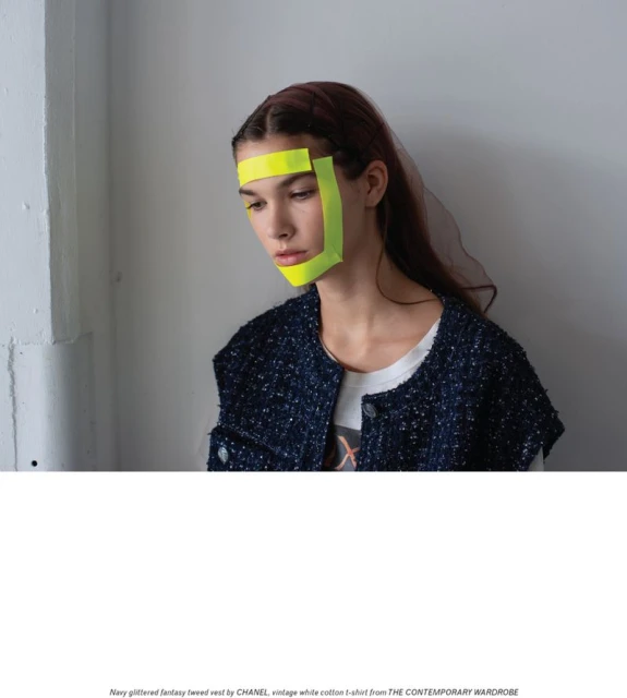 Model wearing a navy tweed vest and neon tape in a studio with natural lighting. Fashion editorial style. Studio shot with copy space.