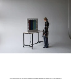 Model standing facing a vanity mirror table against a plain white studio backdrop.