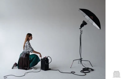 Model kneeling in studio touching a power pack next to a lighting umbrella, for Pop Magazine.