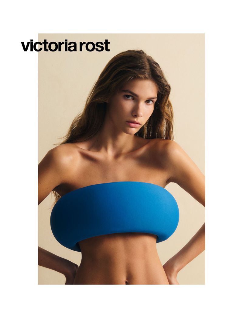 Close-up shot of a female model wearing a blue strapless top by Victoria Rost against a neutral backdrop. Beauty and fashion concept.