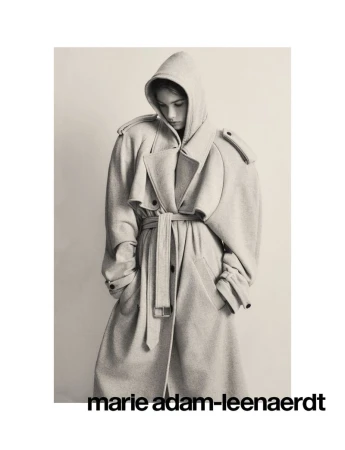 Monochromatic portrait of a woman wearing a belted, hooded trench coat in a studio setting, fashion photography.
