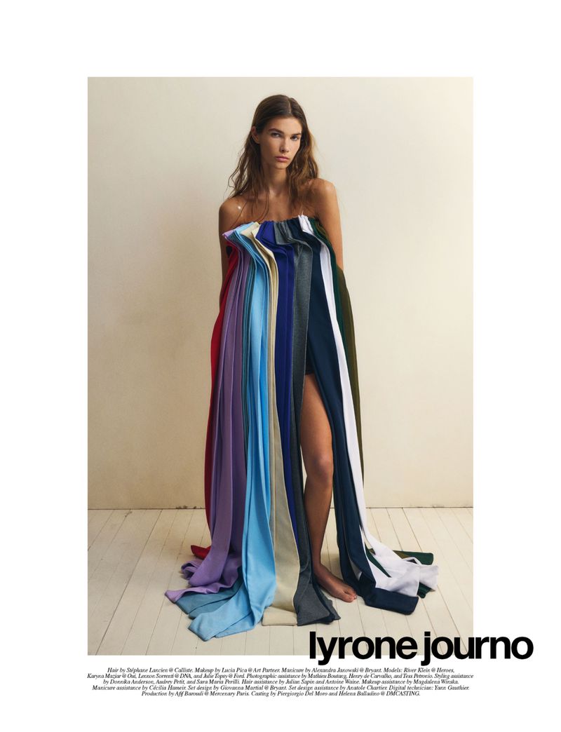Fashion editorial shot of a woman in a colorful draped garment, styled with bare shoulders and neutral background, artistic and posed.