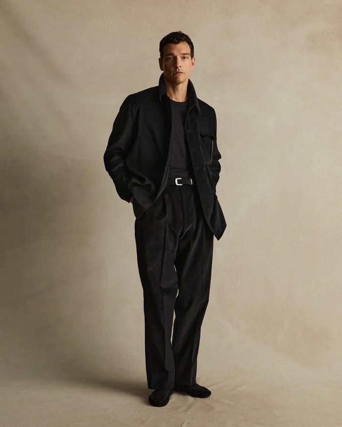 Full-length shot of a man in a black corduroy shirt jacket, black pants, and black shoes, posing in front of a neutral backdrop.
