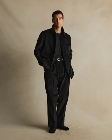 Full-length shot of a man in a black corduroy shirt jacket, black pants, and black shoes, posing in front of a neutral backdrop.