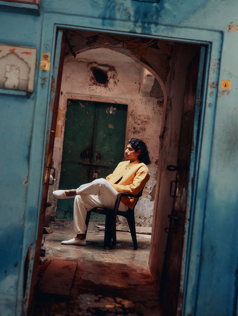 Adult sits on a black chair in front of a green door, framed by a weathered blue doorway, creating a unique indoor setting.