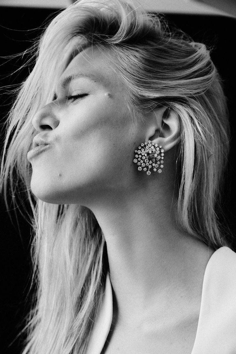 Close-up black and white portrait of a blonde adult female model with an earring and her eyes closed making a kiss face expression.