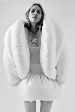 Model wearing a white sculptural padded garment and statement necklace against a plain white background