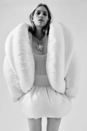 Model wearing a white sculptural padded garment and statement necklace against a plain white background