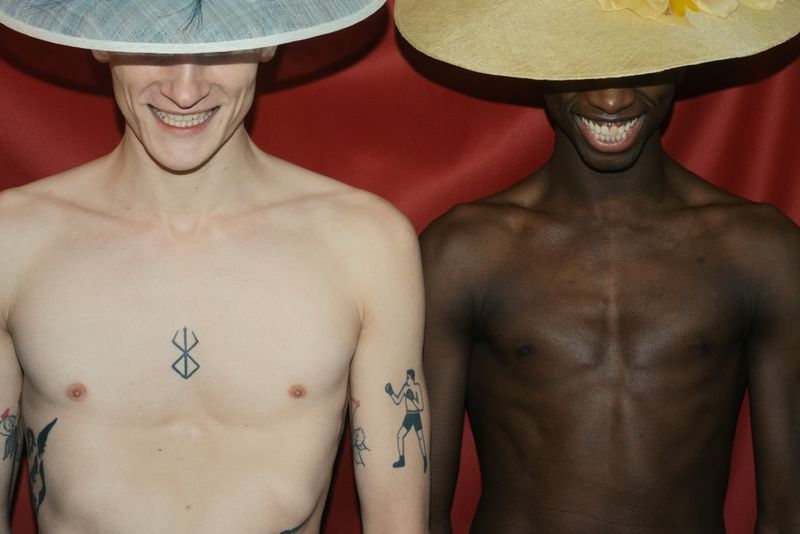 Two shirtless male models wearing wide-brimmed hats against a deep red backdrop for Première Classe by The Greatest Magazine.