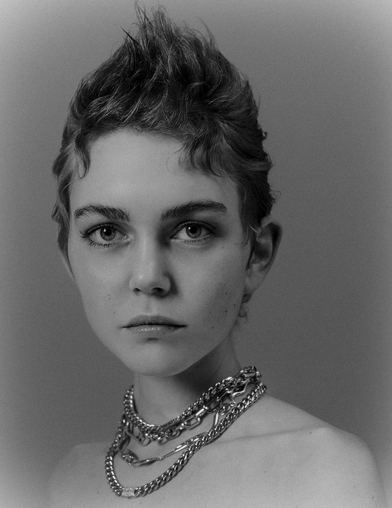 Close-up portrait of a model with short textured hair wearing layered silver chain necklaces against a neutral studio backdrop