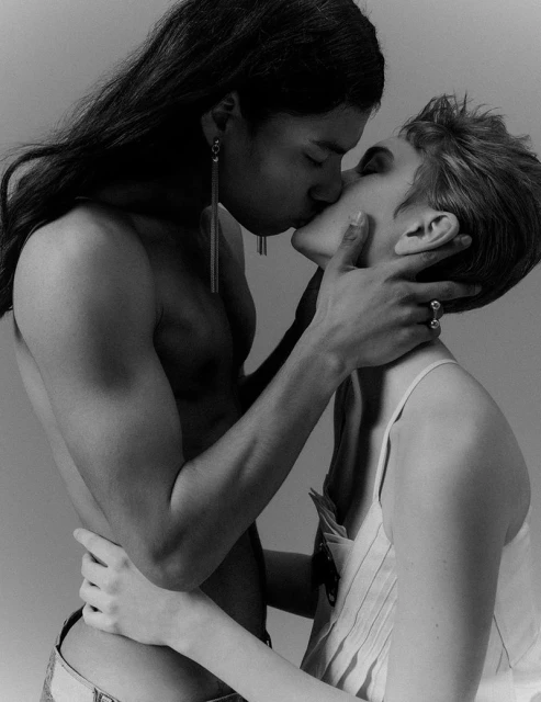 Black and white portrait of two adults in close embrace, face-to-face, with one hand on neck, neutral background, portrait orientation.