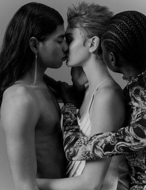 Black and white portrait of four adults of different ethnicities, two kissing, one bare-chested, close up, studio setting.
